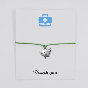 Close-up of winged tooth charm bracelet on white thank you card with green cord.