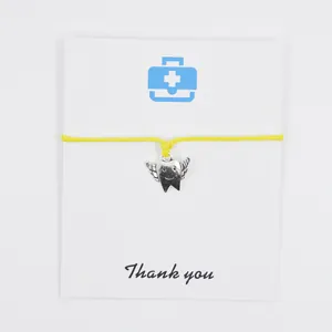 Close-up of angel tooth charm bracelet on a 'Thank you' card with yellow wax cord.