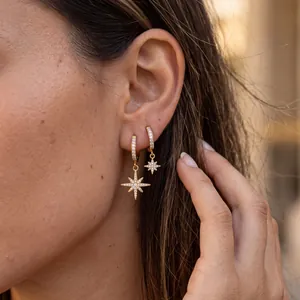 Close-up of sparkling 18k gold plated stainless steel star charm earrings worn by model.