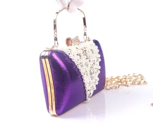 Detailed side view of a purple evening clutch held by hand, showing pearl embellishments