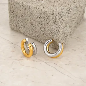 Nahaufnahme von minimalistischen zweifarbigen Gold- und Silber-Ohrklemmen auf Stein.
