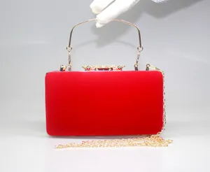 Close-up of red velvet evening clutch bag with elegant gold crown clasp and handle.