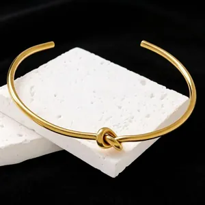 Close-up detail of a minimalist gold-plated titanium steel knot cuff bracelet on white stone