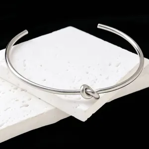 Close-up of a minimalist silver titanium steel knot cuff bracelet on white stone