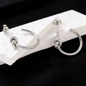 Close-up detail of minimalist titanium steel silver knot hoop earrings on white stone