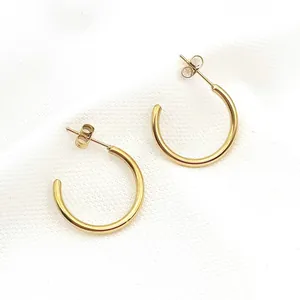 Detailed close-up of minimalist golden stainless steel C-shaped hoop earrings on white fabric