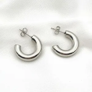 Detailed view of polished stainless steel chunky C-shaped hoop earrings on white fabric