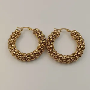 Detalle de pendientes de aro de acero inoxidable dorado con diseño de cuentas único y moderno.