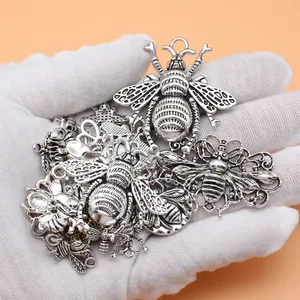 Set mit antiken silbernen Bienenanhängern für DIY-Schmuck auf einer behandschuhten Hand