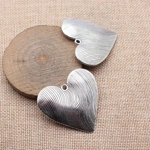 Pendentif cœur en argent antique avec motif ondulé présenté sur un support en bois