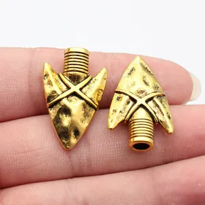 Vintage antique gold arrowhead pendants for DIY jewelry making shown on fingertips for scale