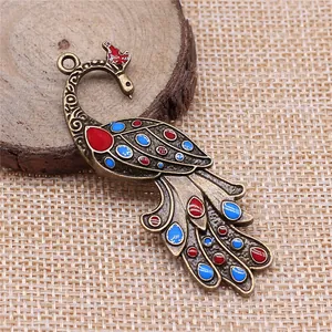 Antique bronze peacock pendant with colorful enamel details on natural woven background.