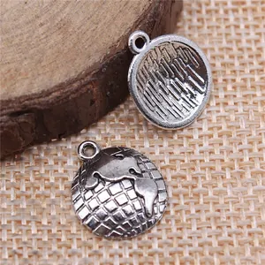 Antique silver globe charms showing front and back patterns on rustic wood