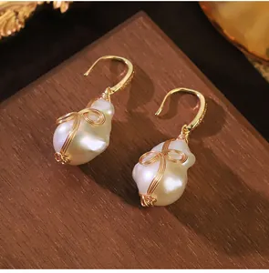 Primer plano de pendientes de perlas barrocas con alambre de oro sobre base de madera