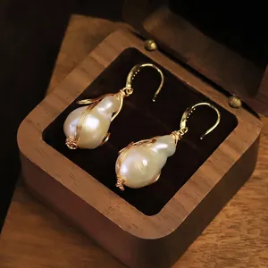 Elegantes pendientes artesanales de perlas barrocas con hilo de oro en joyero de madera vintage