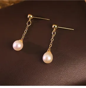 Primo piano dei dettagli di orecchini a goccia con perle d'acqua dolce e catena d'oro.