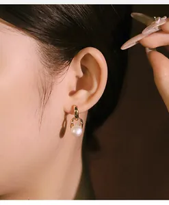 Dettaglio di un orecchino a maglia d'oro con perla naturale indossato da una modella.