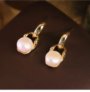 Macro dettagliata di eleganti orecchini a perno in oro a catena con perle bianche tonde