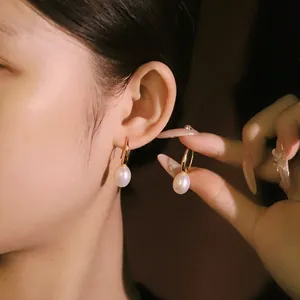 Eleganti orecchini con perle d'acqua dolce naturali e cerchi dorati su una modella.