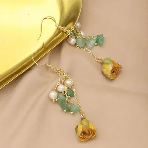 Detail view of long gold earrings with natural pearls, green stones, and dried roses.