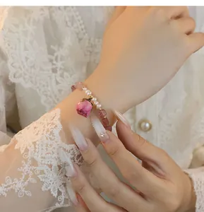 Detalle de una pulsera hecha a mano de cuarzo fresa con perla y un colgante de rosa preservada