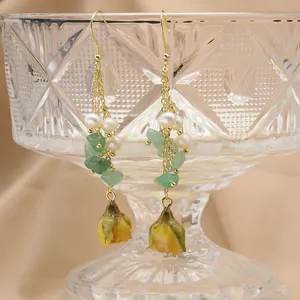 Close-up of long drop earrings featuring white pearls and yellow dried flower buds
