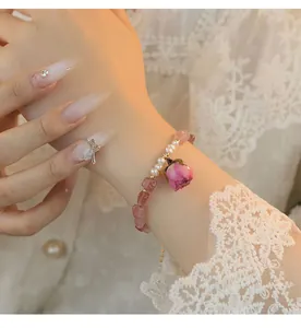 Detalle de una pulsera hecha a mano con cuarzo fresa, perlas y dije de rosa preservada rosa