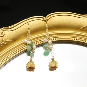 Close-up detail of long freshwater pearl earrings with green stones and flower buds