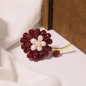 Close-up of red agate flower brooch featuring freshwater pearls and a gold metallic stem.