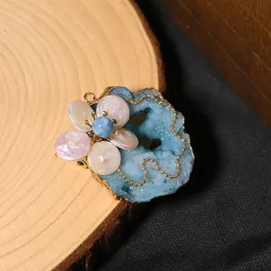 Close-up of handmade brooch with blue druzy crystal and baroque pearl flower details.