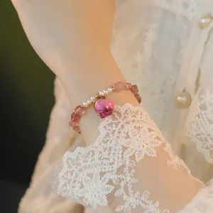 Pulsera artesanal de cuarzo fresa y perlas con dije de capullo de rosa rosa en muñeca.