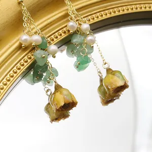 Detailed view of long earrings with natural pearls, green stones, and flower buds