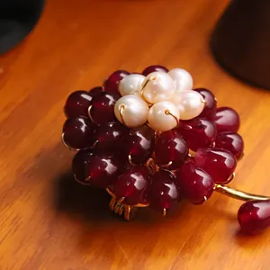 Elegant handmade red agate flower brooch with freshwater pearl accents on a wooden surface