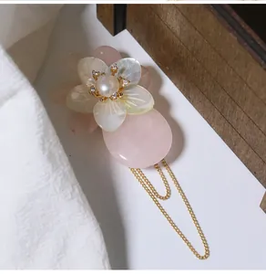 Detailansicht einer rosa Muschelblumenbrosche mit Perle und goldenen Quasten