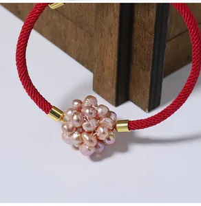 Macro view of a red woven rope bracelet featuring a pink pearl cluster ball