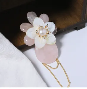 Detailansicht einer eleganten rosa Muschelblumenbrosche mit Perle und goldenen Quasten.