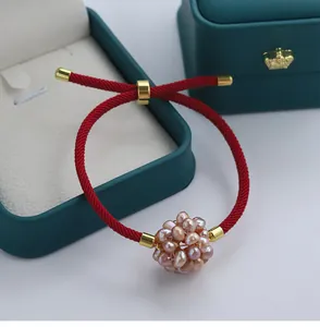 Detailed close-up of a red braided string lucky bracelet with a pink pearl flower ball ornament