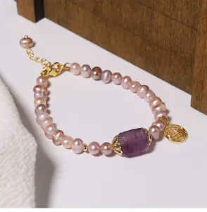 Detailed view of a purple freshwater pearl bracelet with amethyst bead and gold Fu charm.