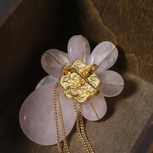 Eleganter rosa Blumen-Brosche mit goldenen Quasten und Muscheldetail in einer Holzkiste
