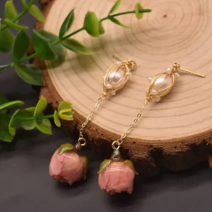 Dettaglio di orecchini pendenti eleganti con perle in gabbia e boccioli di rosa in resina rosa.