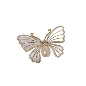 Elegante gouden vlinderbroche met witte schelpvleugels en een natuurlijke zoetwaterparel