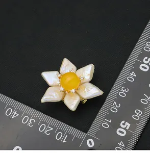 Detailed view of handmade pearl sunflower brooch with yellow jade center next to ruler