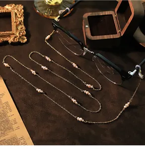 Gedetailleerde close-up van een gouden brillenketting met elegante natuurparels op donkere achtergrond