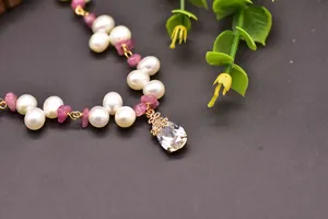 Close-up detail of white freshwater pearls and pink tourmaline on a gold pendant necklace