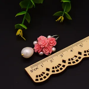 Détail macro d'une boucle d'oreille faite main en fleur de rose et perle près d'une règle