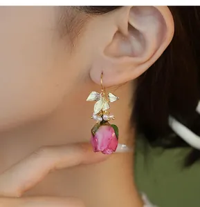 Détail d'une boucle d'oreille en résine rose avec des feuilles dorées et des perles