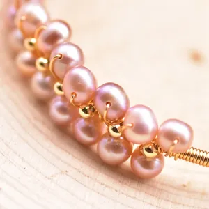 Macro detail of handmade wire wrapped pink freshwater pearl bracelet on wooden background
