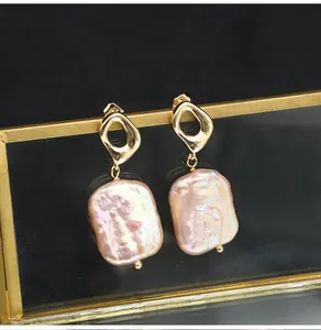 Close-up of elegant gold geometric earrings featuring pink iridescent square baroque pearls