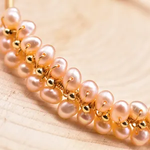 Macro detail of a handmade wire-wrapped natural peach freshwater pearl and gold bead bracelet.