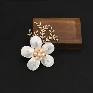 Vista detallada de un broche de flor de nácar con perlas rosas y detalles de hojas doradas